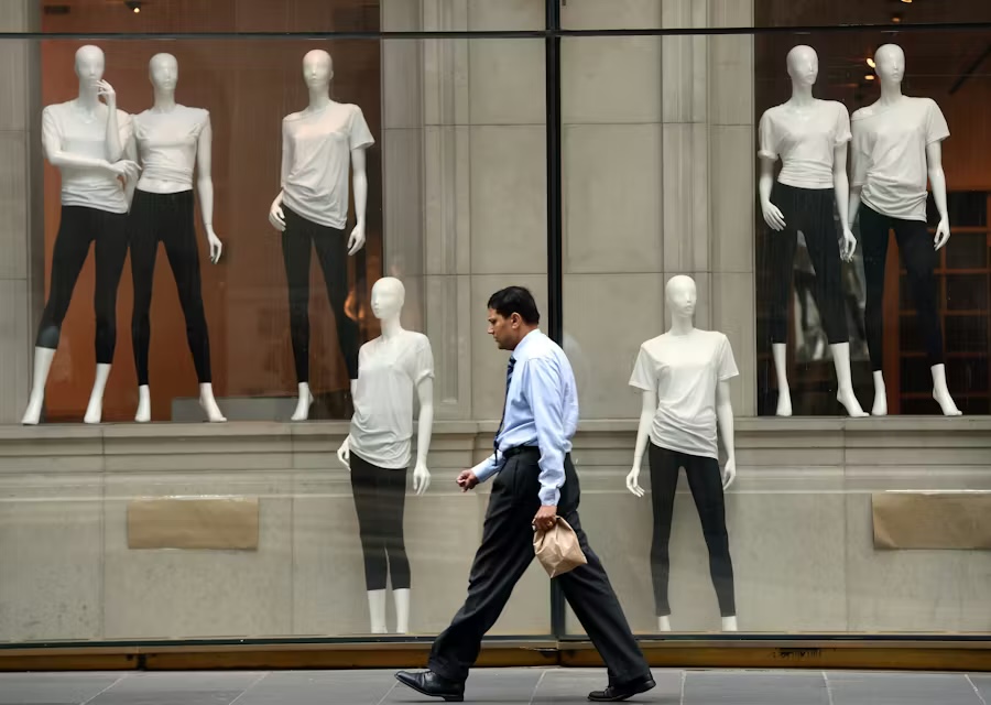 Businessman walking past a department store window displaying white faceless mannequins wearing T-shirts